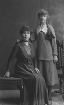 Elderly woman and young girl with long pleated ponytail, possibly mother and daughter.#