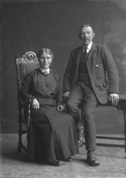 Senior couple, woman seated in chair, man on table.#     