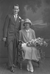 Gardener, bridal couple, he in tails, she seated with bouquet of flowers.