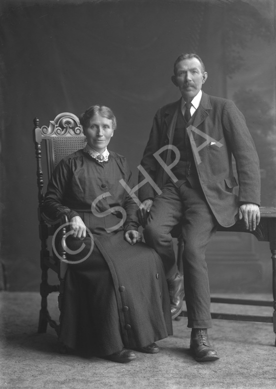 Senior couple, woman seated in chair, man on table.#     