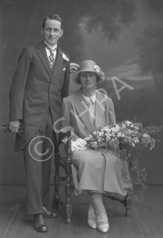Gardener, bridal couple, he in tails, she seated with bouquet of flowers.