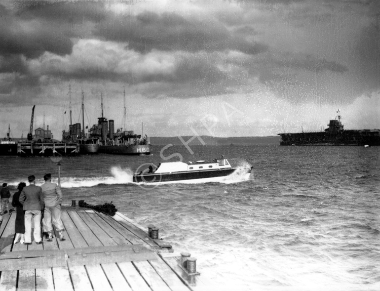 People at Invergordon queuing to take a trip by speedboat to the wreck of the HMS Natal c1932-1938. The H60 was a 'C' Class Destroyer built in 1932 and named HMS Crusader. (She was renamed HMCS Ottawa in 1938). At far right is the aircraft carrier HMS Courageous.*