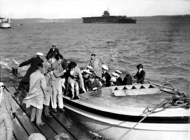 People at Invergordon after taking a trip by speedboat to the wreck of the HMS Natal c1932-1938. The H60 was a 'C' Class Destroyer built in 1932 and named HMS Crusader. (She was renamed HMCS Ottawa in 1938). At far right is the aircraft carrier HMS Courageous.*